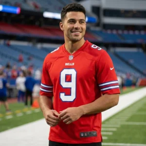 A smiling young man wearing a red Buffalo Bills Color Rush jersey with the number 9 standing in an NFL stadium.