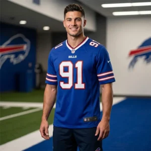 A smiling man wearing a blue Buffalo Bills Ed Oliver number 91 jersey in a locker room setting.