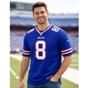 A smiling man wearing a royal blue Buffalo Bills home jersey with the number 8, standing in a blurred football stadium.
